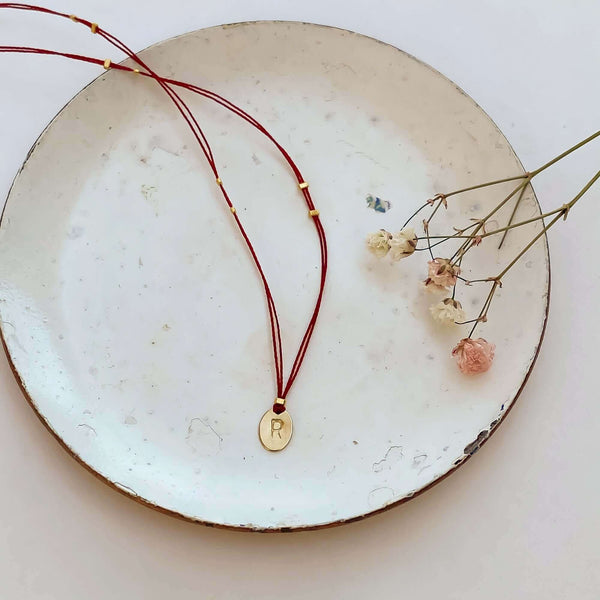 Delicate red thread necklace with gold accents and oval pendant on small plate.