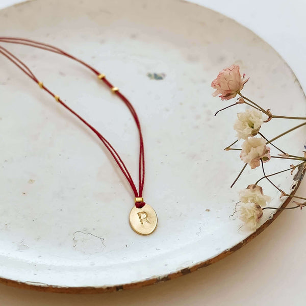 Delicate red thread necklace with gold accents and oval pendant on small plate.