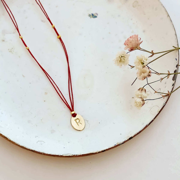 Delicate red thread necklace with gold accents and oval pendant on small plate.