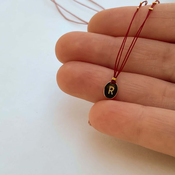 Close-up of fingers with delicate red thread necklace with gold accents and oval pendant.