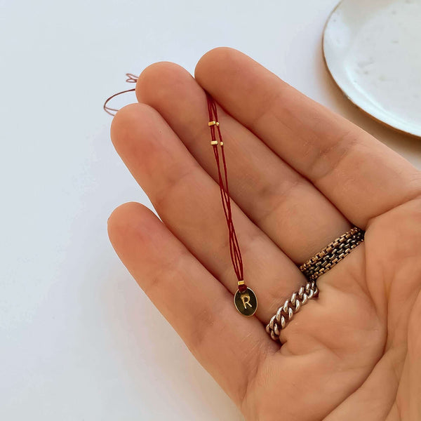 Close-up of fingers with delicate red thread necklace with gold accents and oval pendant.