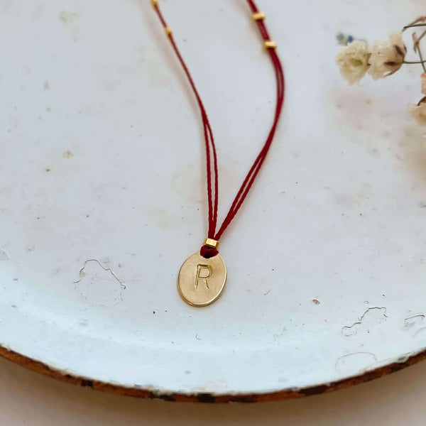 Delicate red thread necklace with gold accents and oval pendant on small plate.
