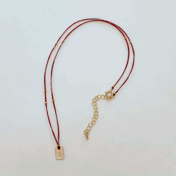 Delicate red thread necklace with gold accents and square pendant.