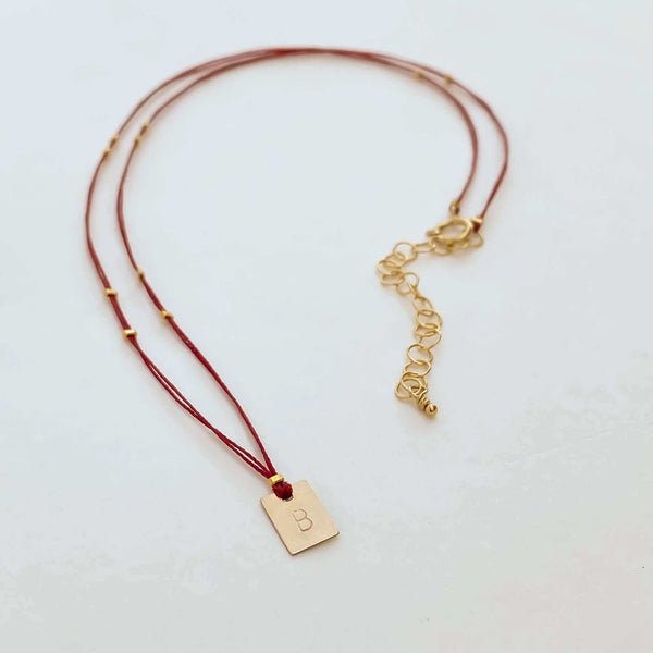Delicate red thread necklace with gold accents and square pendant.