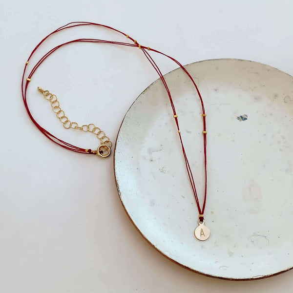 Delicate red thread necklace with gold accents and round pendant on small plate.