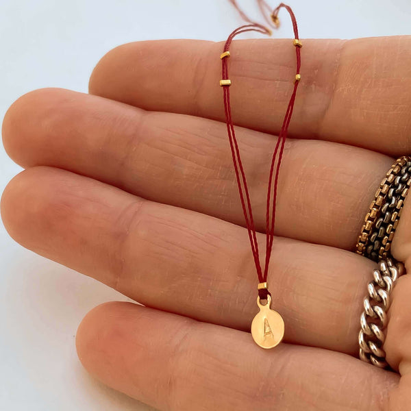 Close-up of fingers with delicate red thread necklace with gold accents and round pendant.