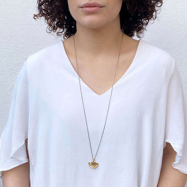 Woman wearing delicate dark chain necklace with tiny gold beads along chain and gold half-circle shaped pendant.