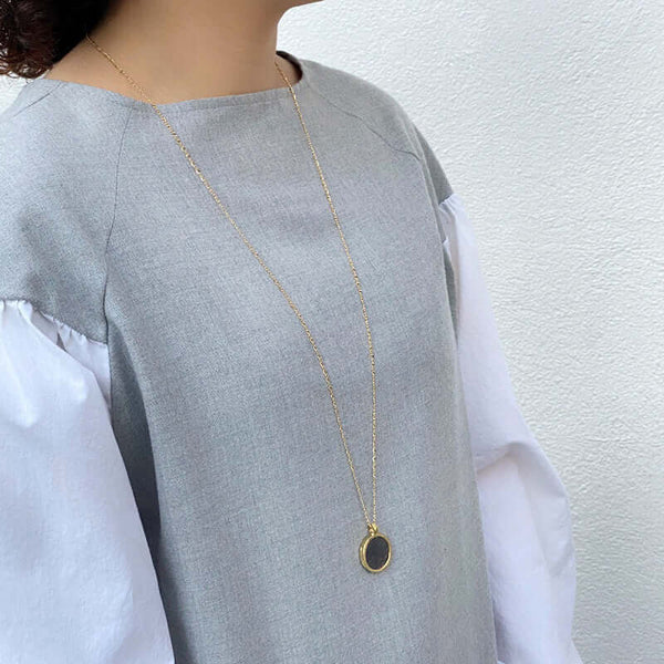 Woman wearing long gold chain necklace with etched coin shaped pendant.