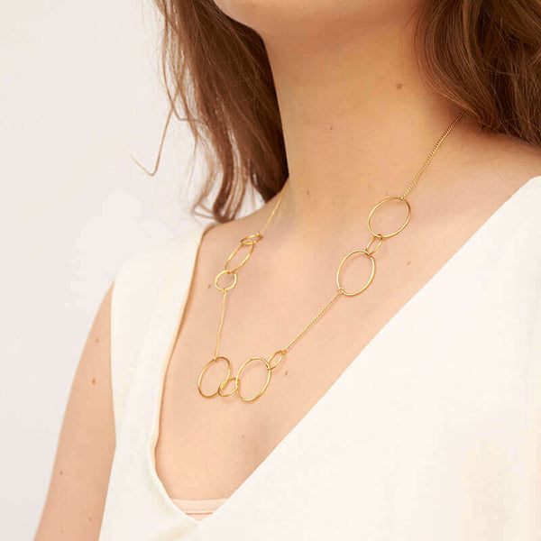 Woman wearing a gold necklace, groups of gold hoops on gold chain, shown side angle.