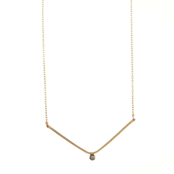 Close-up of delicate gold chain necklace, wide v pendant with dark pearl in middle.