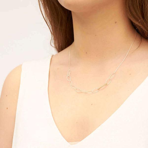 Woman wearing a silver chain necklace with wide oval links in front with detail on 2 gold links, shown side angle.