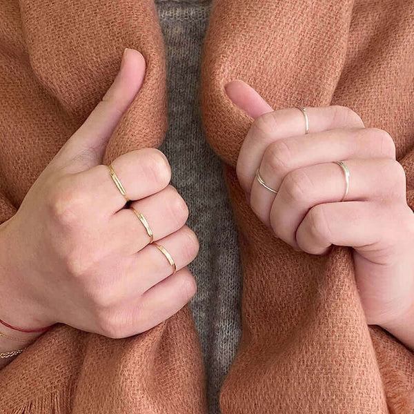 Close-up of two hands wearing various gold and silver hand-hammered rings.