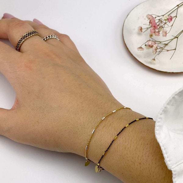 Close-up of wrist wearing a gold and a silver delicate chain bracelet, both with silver rectangular bead accents.