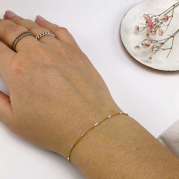 Close-up of wrist wearing delicate gold chain bracelet, with silver rectangular bead accents.