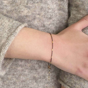 Close-up of wrist wearing delicate black chain bracelet, with gold rectangular bead accents.