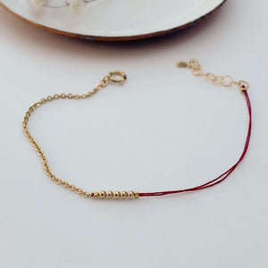 Delicate bracelet of gold chain and red thread with gold beads detail at center.