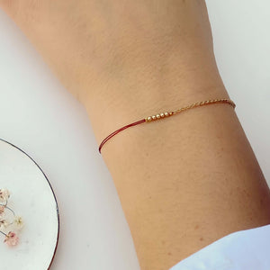 Close-up of hand wearing delicate bracelet of gold chain and red thread with gold beads detail at center.