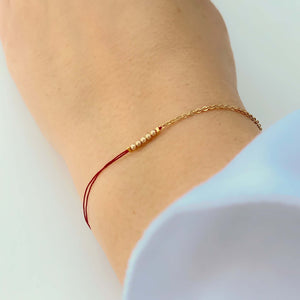 Close-up of hand wearing delicate bracelet of gold chain and red thread with gold beads detail at center.