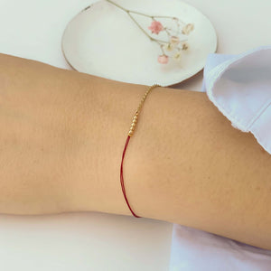 Close-up of hand wearing delicate bracelet of gold chain and red thread with gold beads detail at center.