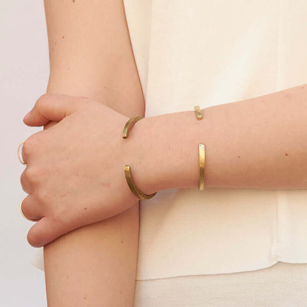 Close-up of arm wearing a brass and a silver hand-hammered open cuff bracelet, showing the open side.