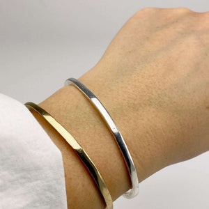 Close-up of wrist wearing a brass and a silver hand-hammered open cuff bracelet.