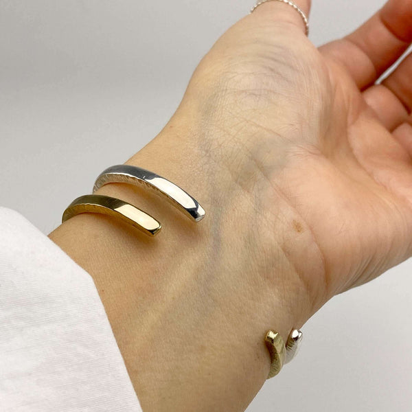 Close-up of wrist wearing a brass and a silver hand-hammered open cuff bracelet, showing the open side.