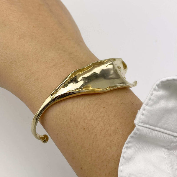 Close-up of hand wearing open cuff polished white bronze bracelet with organic leaf motif.