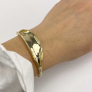 Close-up of hand wearing open cuff polished brass bracelet with organic leaf motif.