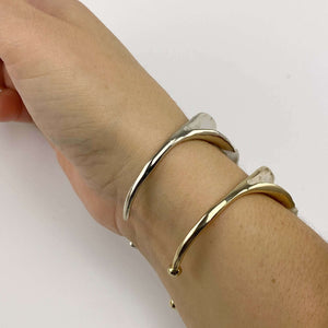 Close-up of hand wearing a polished white bronze and a polished brass open cuff bracelet with organic leaf motif.