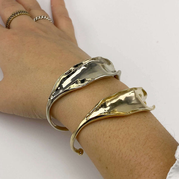 Close-up of hand wearing a polished white bronze and a polished brass open cuff bracelet with organic leaf motif.
