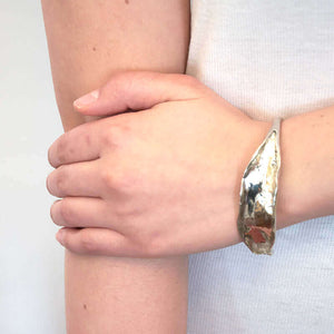 Close-up of arm wearing open cuff polished white bronze bracelet with organic leaf motif.