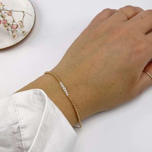 Close-up of hand wearing gold beaded bracelet with pearls at the center and adjustable sliding clasp.