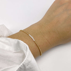 Close-up of hand wearing gold beaded bracelet with pearls at the center and adjustable sliding clasp.