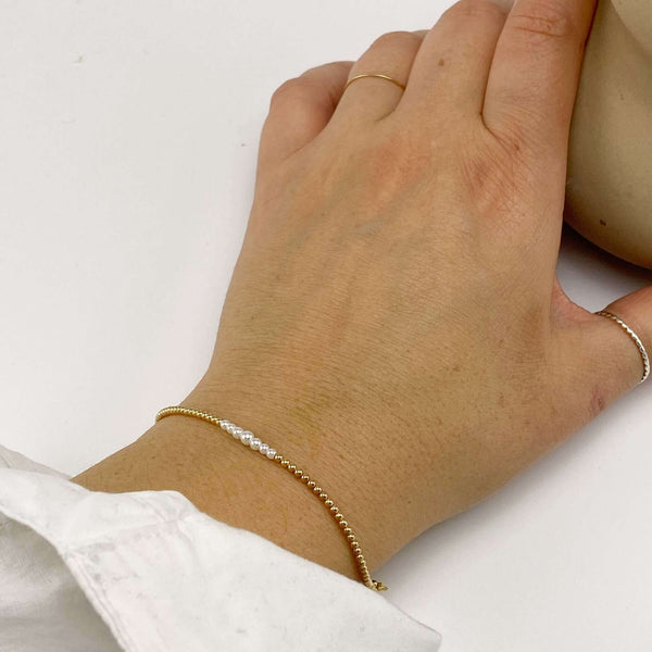 Close-up of hand wearing gold beaded bracelet with pearls at the center and adjustable sliding clasp.