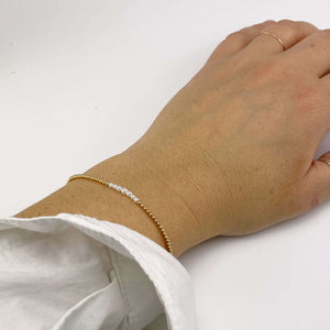 Close-up of hand wearing gold beaded bracelet with pearls at the center and adjustable sliding clasp.