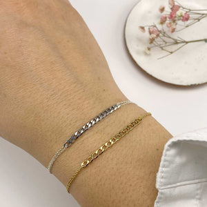 Close-up of hand wearing a gold and a silver delicate chain bracelet with curb chain detail at center.