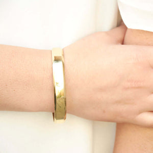 Close-up of hand wearing heavy cuff bracelet with chamfered edges and overlapping ends, in polished brass.