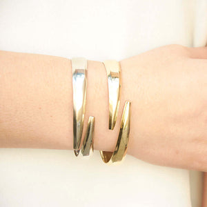 Close-up of hand wearing 2 heavy cuff bracelet with chamfered edges and overlapping ends, in polished white bronze and polished brass.