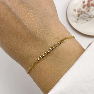 Close-up of hand wearing delicate gold chain bracelet with curb chain detail at center.