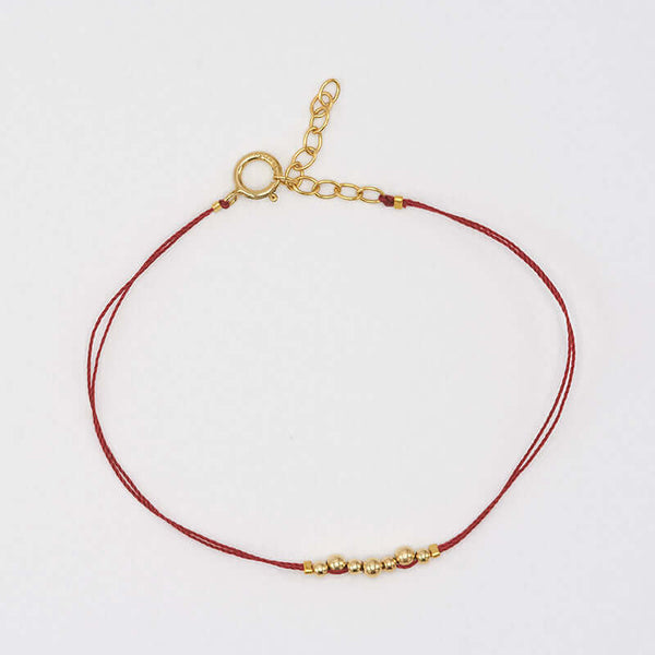 Delicate red thread bracelet with gold beads detail at center.