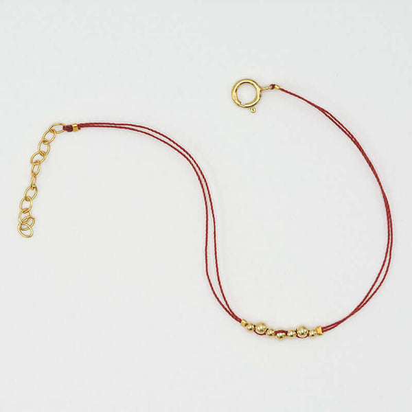 Delicate red thread bracelet with gold beads detail at center.
