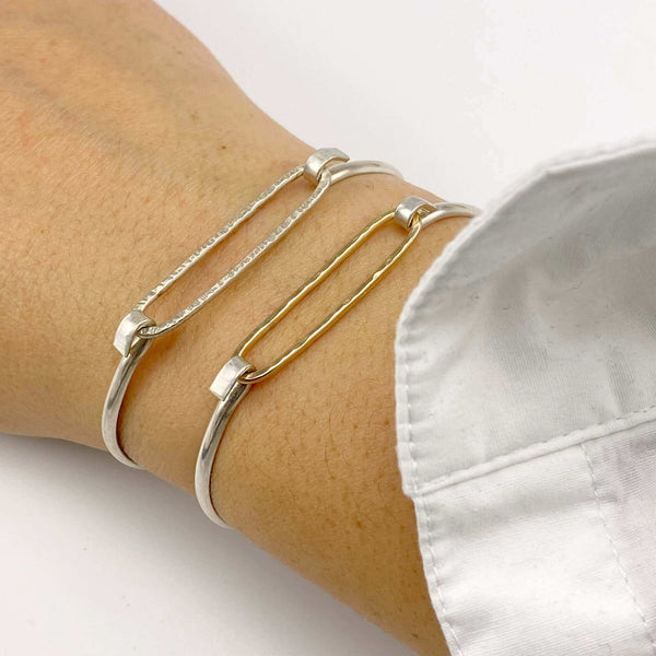 Close-up of hand wearing 2 simple bangle bracelets one with gold and one with silver hammered oval on silver cuff.