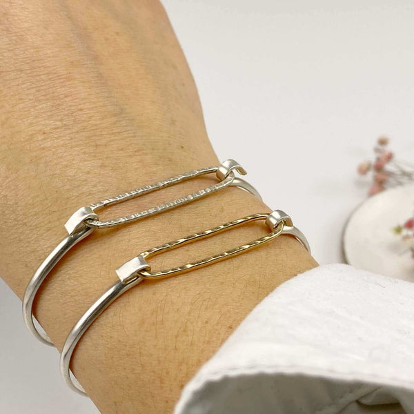 Close-up of hand wearing 2 simple bangle bracelets one with gold and one with silver hammered oval on silver cuff.