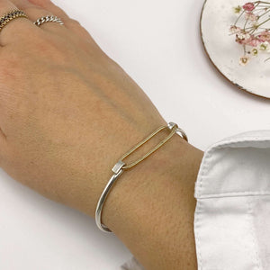 Close-up of hand wearing simple bangle bracelets with gold hammered oval on silver cuff.