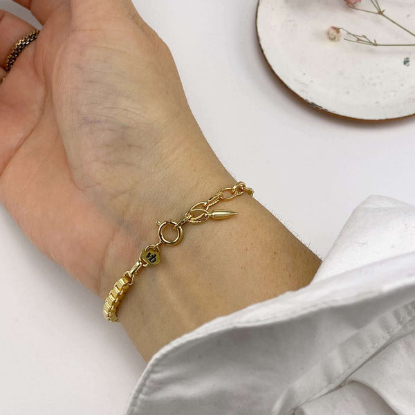 Close-up of hand wearing a chunky gold box chain bracelet, showing clasp.
