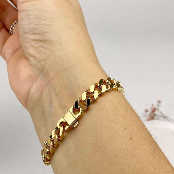 Close-up of hand wearing a chunky gold curb chain bracelet, showing lay flat clasp.
