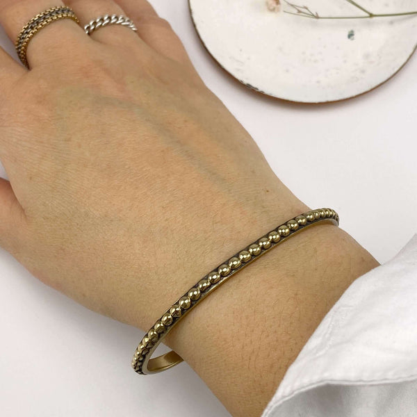 Close-up of hand wearing a polished brass beaded bangle bracelet.