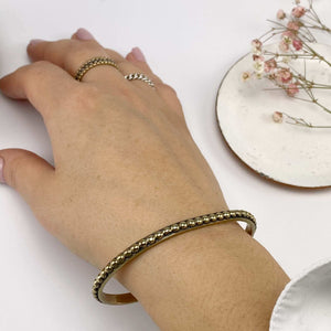 Close-up of hand wearing a polished brass beaded bangle bracelet.