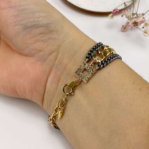 Close-up of hand wearing a uulti-chain bracelet of chunky dark and gold chain, showing clasp detail.
