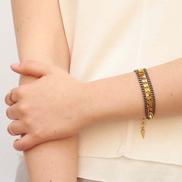 Close-up of arm wearing a uulti-chain bracelet of chunky dark and gold chain.